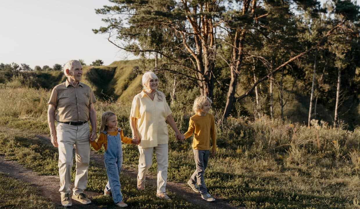 Grands-parents se promenant main dans la main avec leurs petits-enfants dans un cadre naturel verdoyant