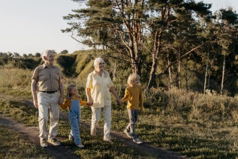 Grands-parents se promenant main dans la main avec leurs petits-enfants dans un cadre naturel verdoyant